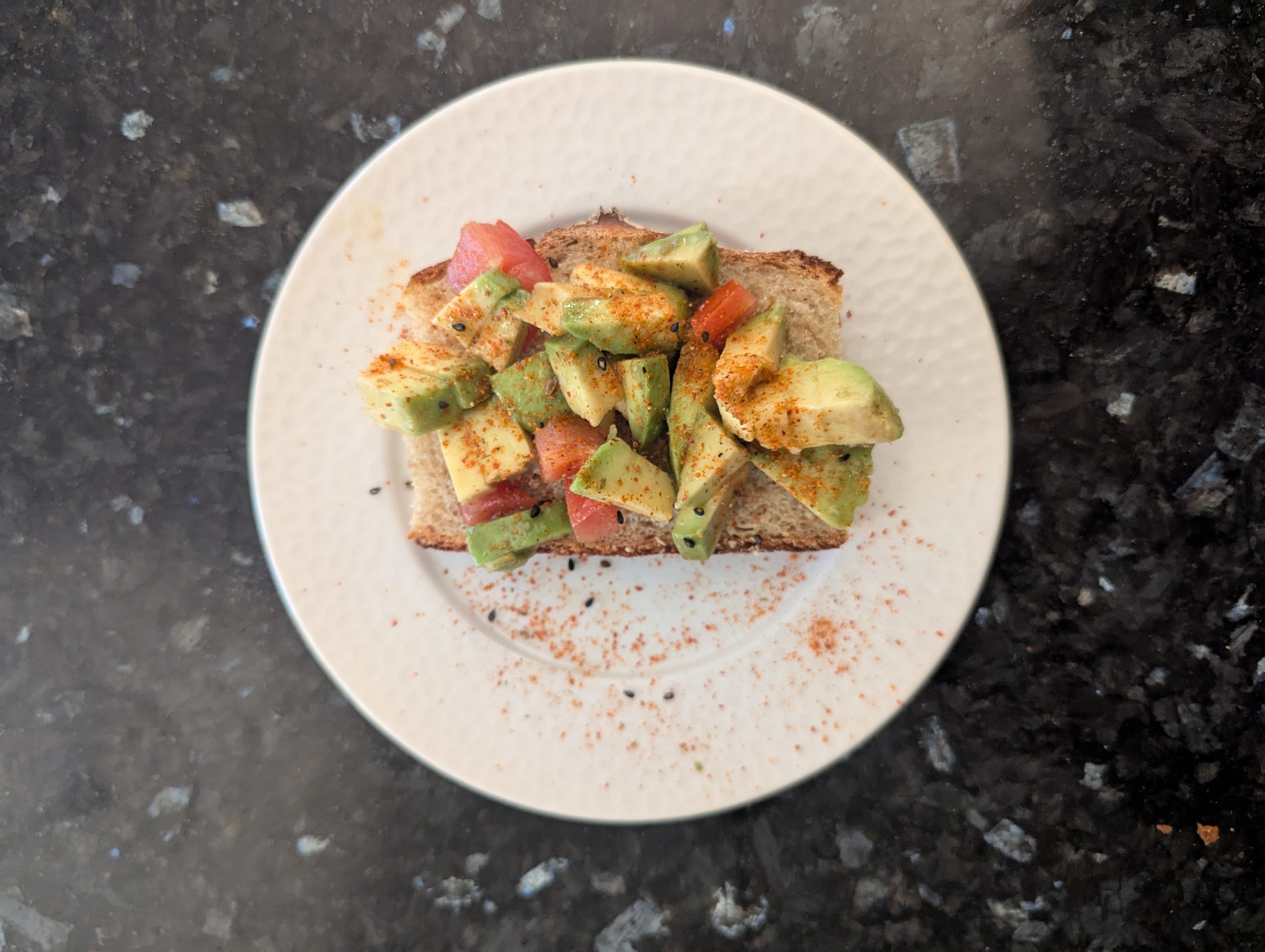 Tartine de pain de campagne grillé garnie d'avocat et tomates en dés avec piment d'Espelette, servie sur une assiette blanche