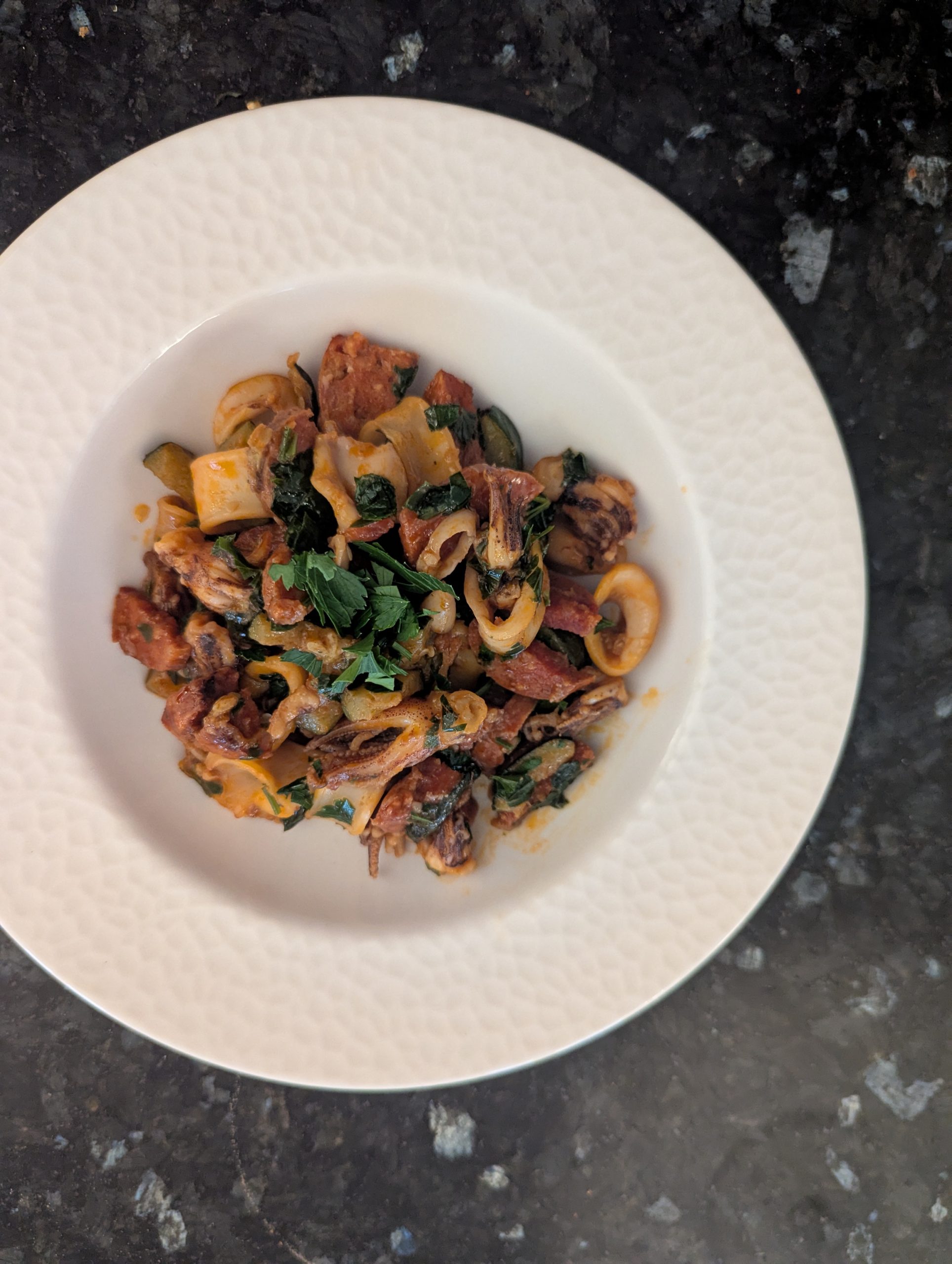 Poêlée de calamar sauté en lamelles avec chorizo et courgette, dressée dans une assiette creuse blanche
