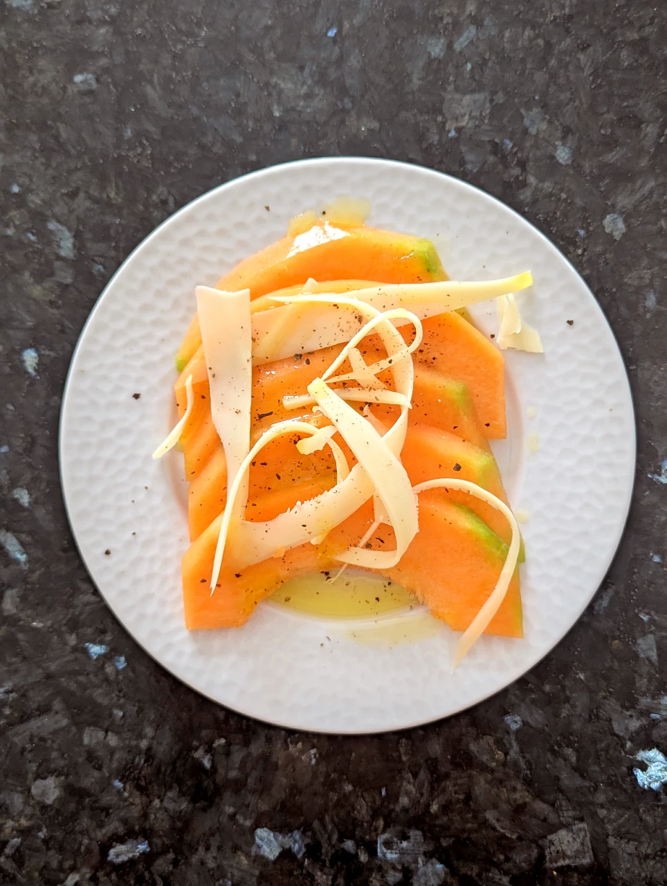 Tranches de melon en demi-lunes avec copeaux de tome de chèvre, filet d'huile d'olive et poivre du moulin